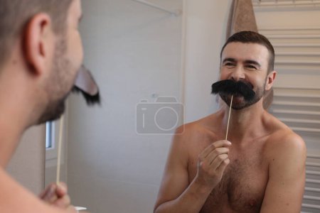 Téléchargez les photos : Portrait de jeune homme avec moustache sur bâton devant miroir dans la salle de bain - en image libre de droit