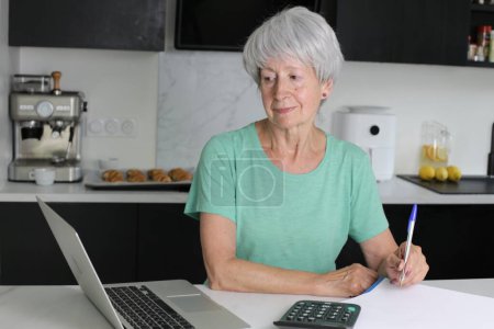 Téléchargez les photos : Portrait en gros plan de femme mature travaillant avec un ordinateur portable à la cuisine - en image libre de droit
