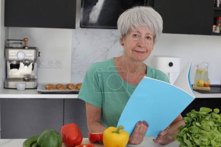 Foto de Primer plano retrato de mujer madura leyendo libro de recetas en la cocina - Imagen libre de derechos