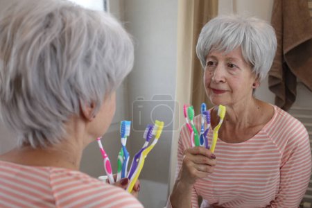 Téléchargez les photos : Portrait en gros plan de femme mature avec brosses à dents devant le miroir dans la salle de bain - en image libre de droit