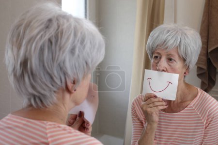 Foto de Primer plano retrato de mujer madura con sonrisa dibujada en papel delante del espejo en el baño - Imagen libre de derechos