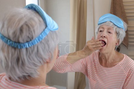 Foto de Primer plano retrato de mujer madura con máscara de dormir delante del espejo en el baño - Imagen libre de derechos