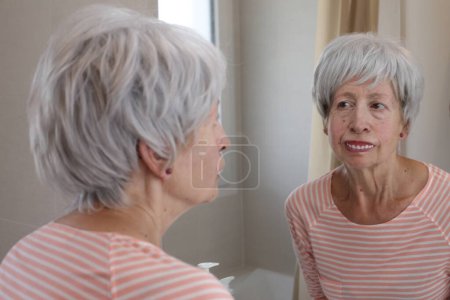 Photo for Close-up portrait of mature woman looking at her teeth in front of mirror in bathroom - Royalty Free Image
