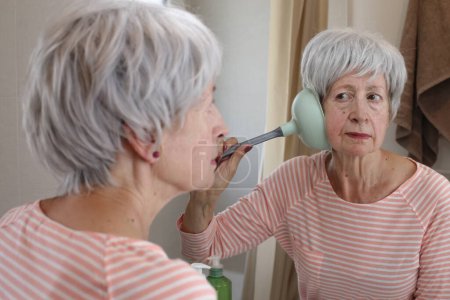 Photo for Close-up portrait of mature woman with plunge on her ear in front of mirror in bathroom - Royalty Free Image