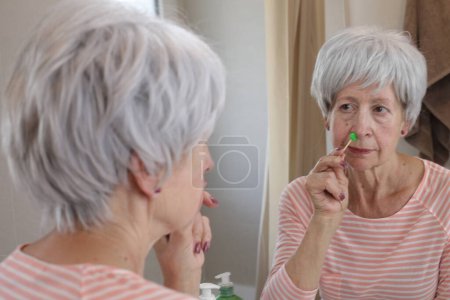 Photo for Close-up portrait of mature woman removing her nose hair with wax in front of mirror in bathroom - Royalty Free Image
