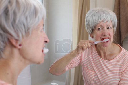 Photo for Close-up portrait of mature woman with bleeding gums while she brushing teeth in front of mirror in bathroom - Royalty Free Image
