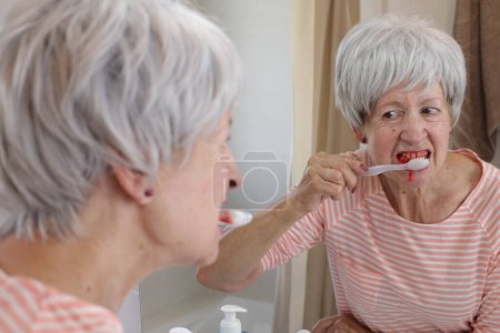 Foto de Retrato de cerca de una mujer madura con encías sangrantes mientras se cepilla los dientes delante del espejo en el baño - Imagen libre de derechos