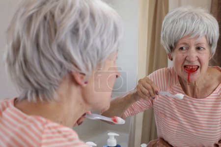 Photo for Close-up portrait of mature woman with bleeding gums while she brushing teeth in front of mirror in bathroom - Royalty Free Image