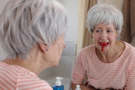 Foto de Primer plano retrato de mujer madura con dientes sangrantes delante del espejo en el baño - Imagen libre de derechos