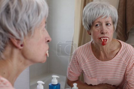 Photo for Close-up portrait of mature woman with vampire teeth in front of mirror in bathroom - Royalty Free Image