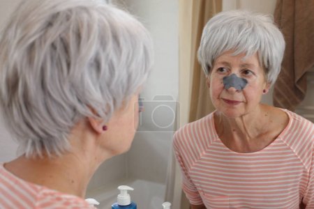 Téléchargez les photos : Portrait en gros plan de femme mature avec patch noir sur le nez devant le miroir dans la salle de bain - en image libre de droit