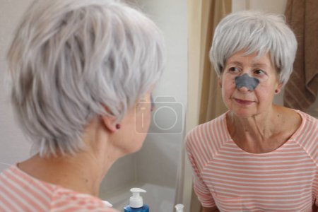 Photo for Close-up portrait of mature woman with black patch on nose in front of mirror in bathroom - Royalty Free Image