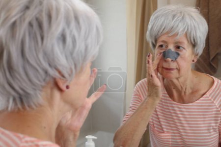 Photo for Close-up portrait of mature woman with black patch on nose in front of mirror in bathroom - Royalty Free Image