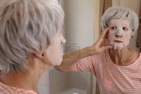 Foto de Primer plano retrato de mujer madura con máscara facial delante del espejo en el baño - Imagen libre de derechos