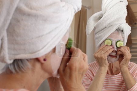 Foto de Primer plano retrato de mujer madura con máscara facial y toalla en la cabeza delante del espejo en el baño - Imagen libre de derechos
