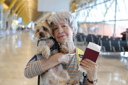 Téléchargez les photos : Portrait en gros plan de femme mature avec passeport et son adorable petit chien à l'aéroport - en image libre de droit