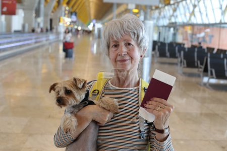 Photo for Close-up portrait of mature woman with passport and her adorable little dog at airport - Royalty Free Image