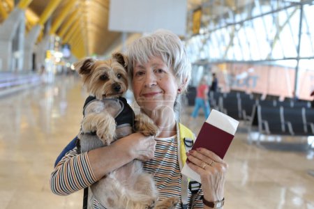 Téléchargez les photos : Portrait en gros plan de femme mature avec passeport et son adorable petit chien à l'aéroport - en image libre de droit