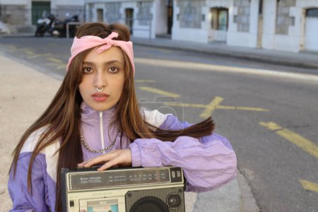 Photo for Portrait of stylish hipster woman wearing headband and piercing holding tape recorder on urban background - Royalty Free Image