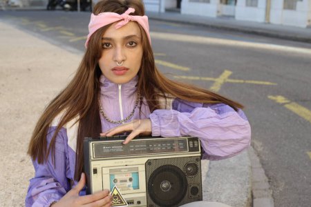 Téléchargez les photos : Portrait de la femme hipster élégant portant bandeau et percing tenant magnétophone sur fond urbain - en image libre de droit