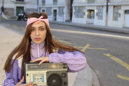Téléchargez les photos : Portrait de la femme hipster élégant portant bandeau et percing tenant magnétophone sur fond urbain - en image libre de droit
