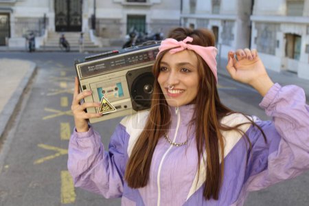 Téléchargez les photos : Élégant hipster femme portant bandeau et percing tenant magnétophone sur fond urbain - en image libre de droit