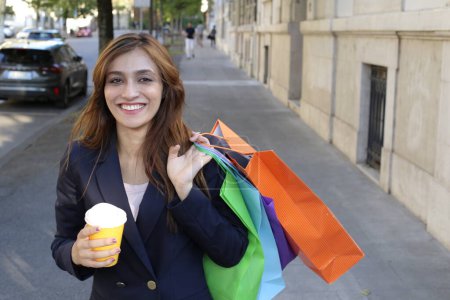 Foto de Mujer de negocios en traje sosteniendo café y bolsas de compras al aire libre - Imagen libre de derechos