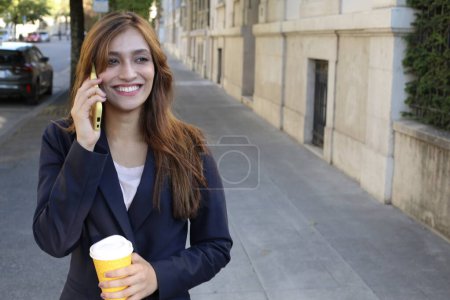 Foto de Mujer de negocios en traje hablando a través de teléfono inteligente y la celebración de café al aire libre - Imagen libre de derechos
