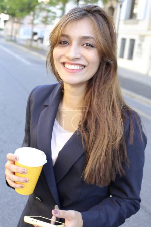 Téléchargez les photos : Femme d'affaires en costume tenant smartphone et café en plein air - en image libre de droit