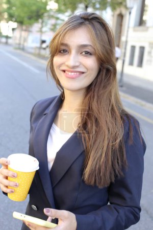 Foto de Mujer de negocios en traje con teléfono inteligente y café al aire libre - Imagen libre de derechos