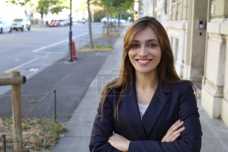 Téléchargez les photos : Femme d'affaires adulte avec les bras croisés posant à l'extérieur souriant à la caméra avec un fond urbain - en image libre de droit