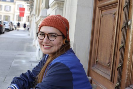 Téléchargez les photos : Portrait de jeune belle femme dans des vêtements hipster élégants avec écouteurs vintage sur la rue de la ville - en image libre de droit