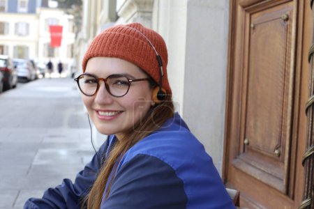 Foto de Retrato de mujer hermosa joven en ropa hipster con estilo con auriculares vintage en la calle de la ciudad - Imagen libre de derechos