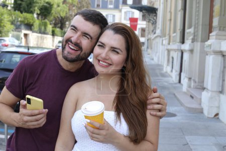 Téléchargez les photos : Portrait de jeune couple heureux avec tasse en papier de café et smartphone sur la rue de la ville ensemble - en image libre de droit