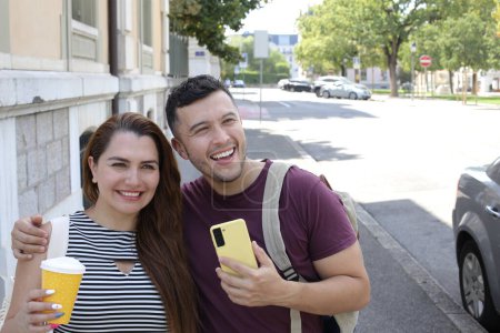 Téléchargez les photos : Portrait de jeune couple heureux avec tasse en papier de café et smartphone sur la rue de la ville ensemble - en image libre de droit