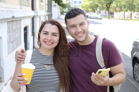 Photo for Portrait of young happy couple with paper cup of coffee and smartphone on city street together - Royalty Free Image