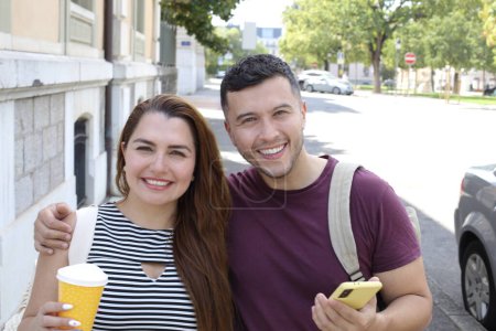 Photo for Portrait of young happy couple with paper cup of coffee and smartphone on city street together - Royalty Free Image