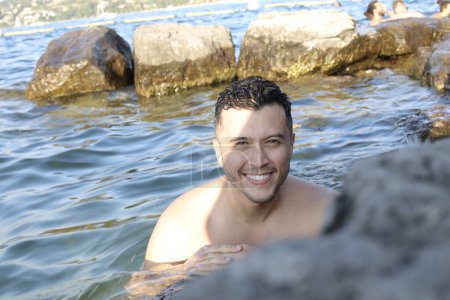 Foto de Retrato de cerca del joven guapo posando en el agua a orillas del mar rocoso - Imagen libre de derechos