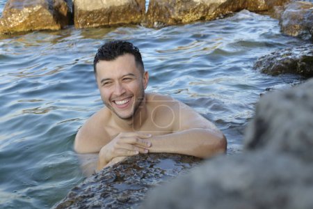 Téléchargez les photos : Portrait en gros plan d'un beau jeune homme posant dans l'eau au bord de la mer rocheuse - en image libre de droit