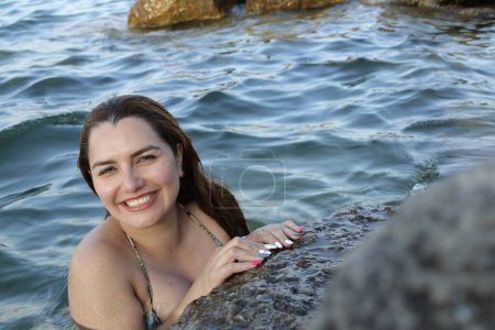 Téléchargez les photos : Portrait en gros plan de belle jeune femme en bikini posant dans l'eau au bord de la mer rocheuse - en image libre de droit