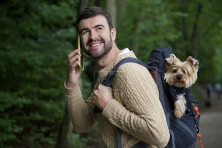 Téléchargez les photos : Portrait de beau jeune homme heureux voyageant avec son chien mignon dans un sac à dos - en image libre de droit