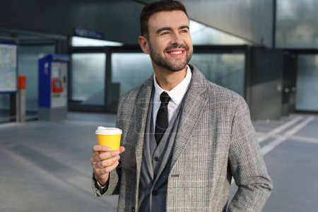 Photo for Portrait of handsome young man in grey suit with paper cup of coffee on city street - Royalty Free Image