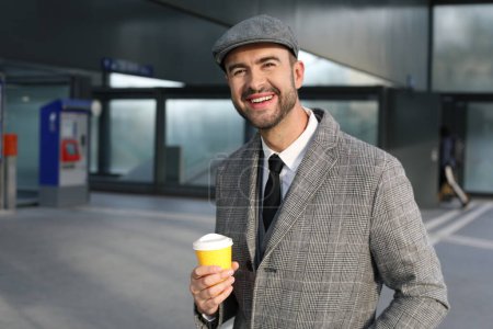 Photo for Portrait of handsome young man in grey suit with paper cup of coffee on city street - Royalty Free Image