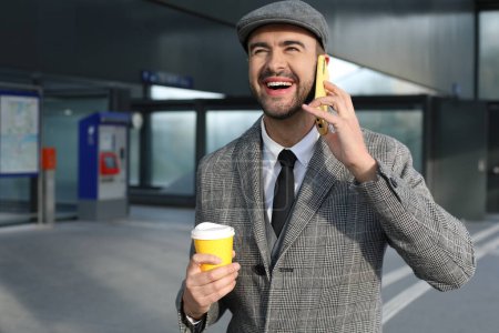 Téléchargez les photos : Portrait de beau jeune homme en costume gris avec tasse de café en papier sur la rue de la ville - en image libre de droit