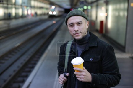 Photo for Portrait of handsome young man in stylish clothes with paper cup of coffee on train station - Royalty Free Image