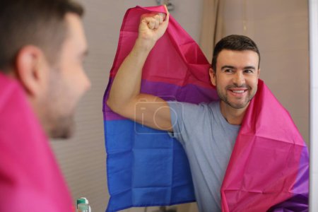 Foto de Retrato de joven guapo con bandera bisexual delante del espejo en el baño - Imagen libre de derechos