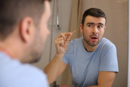 Photo for Portrait of handsome young man cleaning ears in front of mirror in bathroom - Royalty Free Image