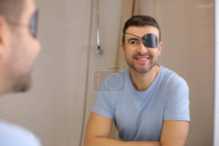 Téléchargez les photos : Portrait de beau jeune homme avec couverture oculaire devant le miroir dans la salle de bain - en image libre de droit