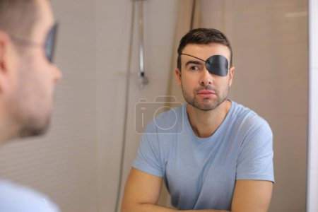 Téléchargez les photos : Portrait de beau jeune homme avec couverture oculaire devant le miroir dans la salle de bain - en image libre de droit