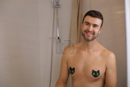Photo for Portrait of handsome young shirtless man with taped nipples in front of mirror in bathroom - Royalty Free Image